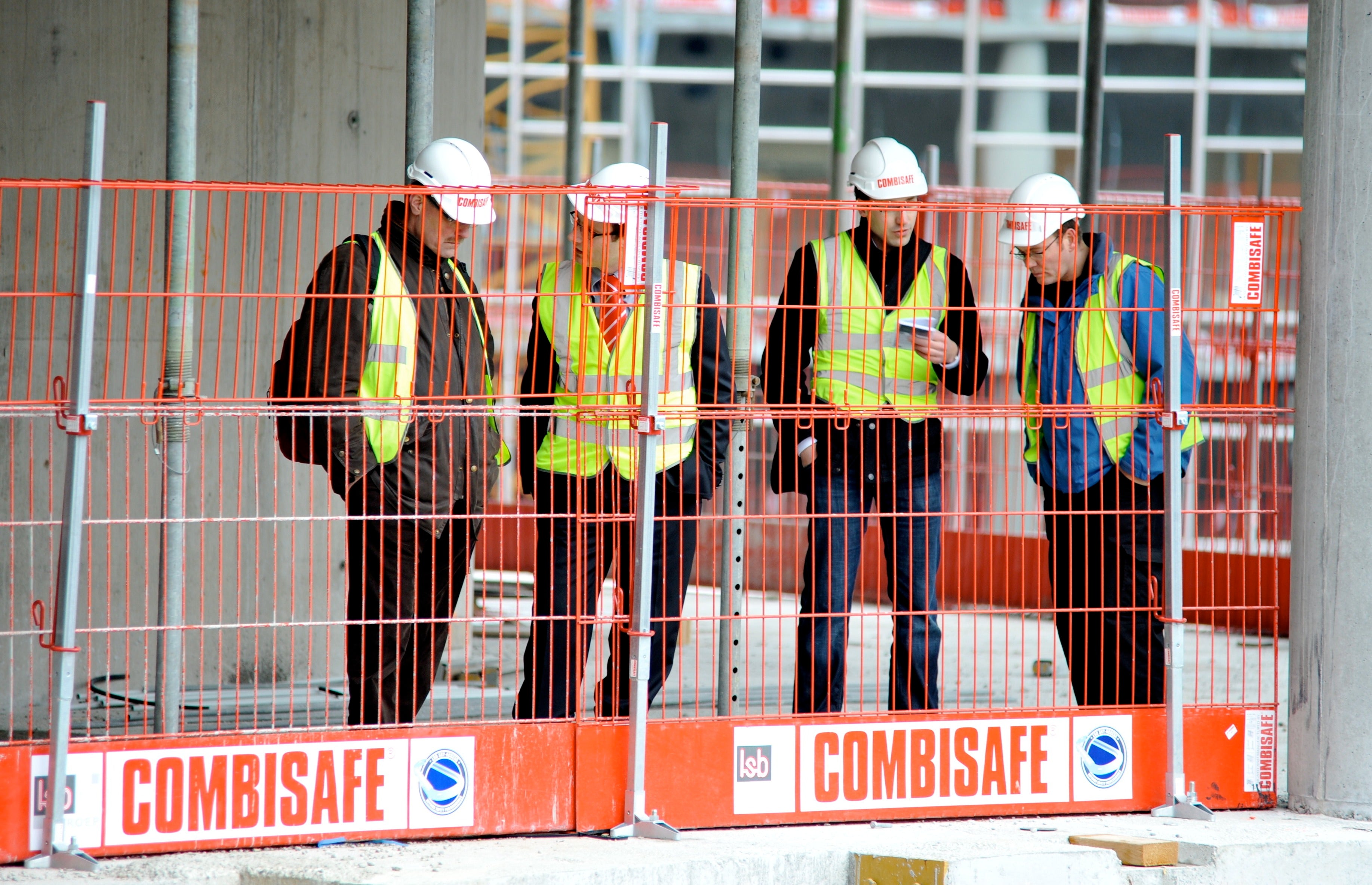 Construction workers behind a red safety fence with 'COMBISAFE' branding.