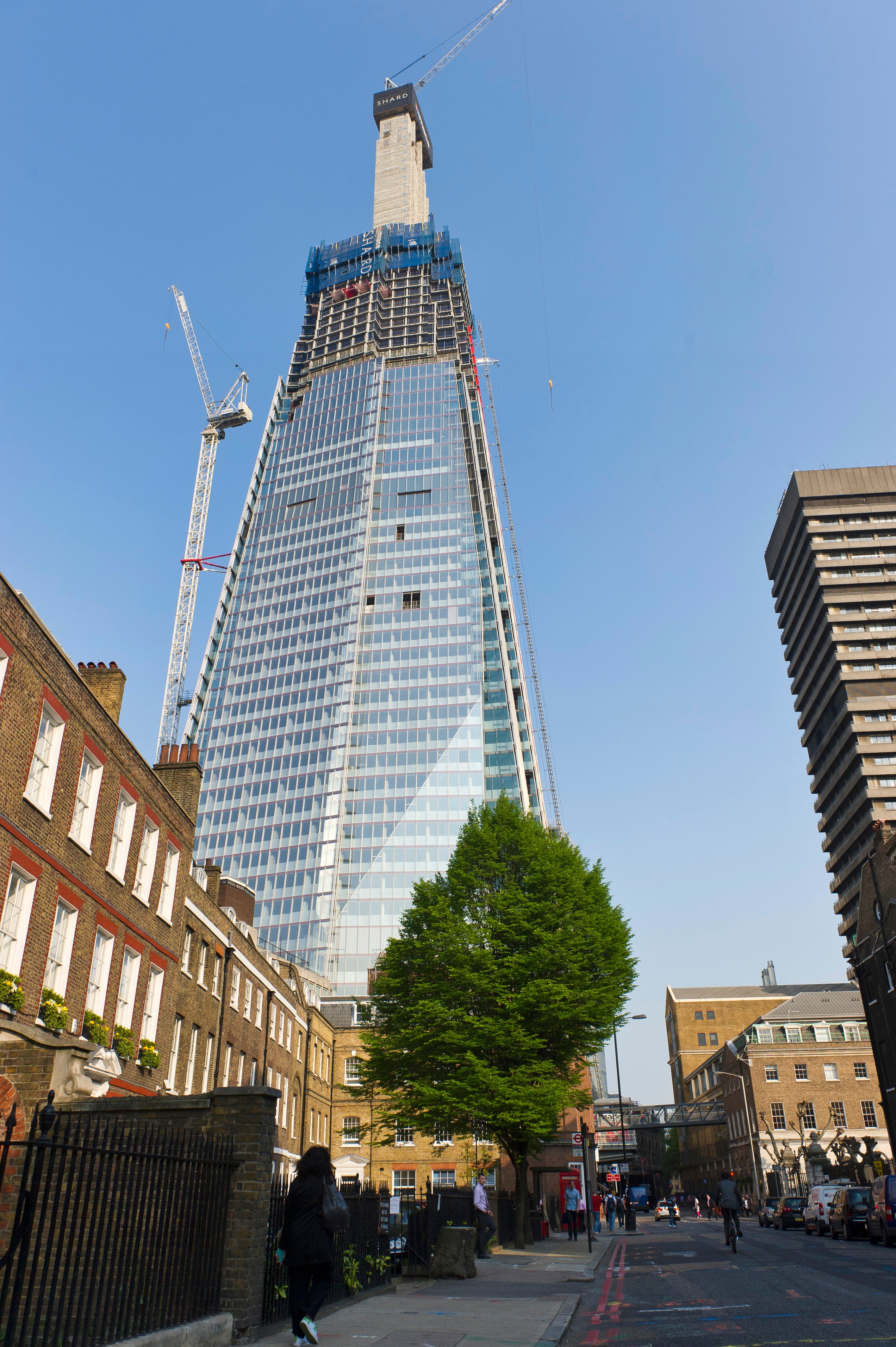 Tall building under construction with cranes against a clear blue sky.