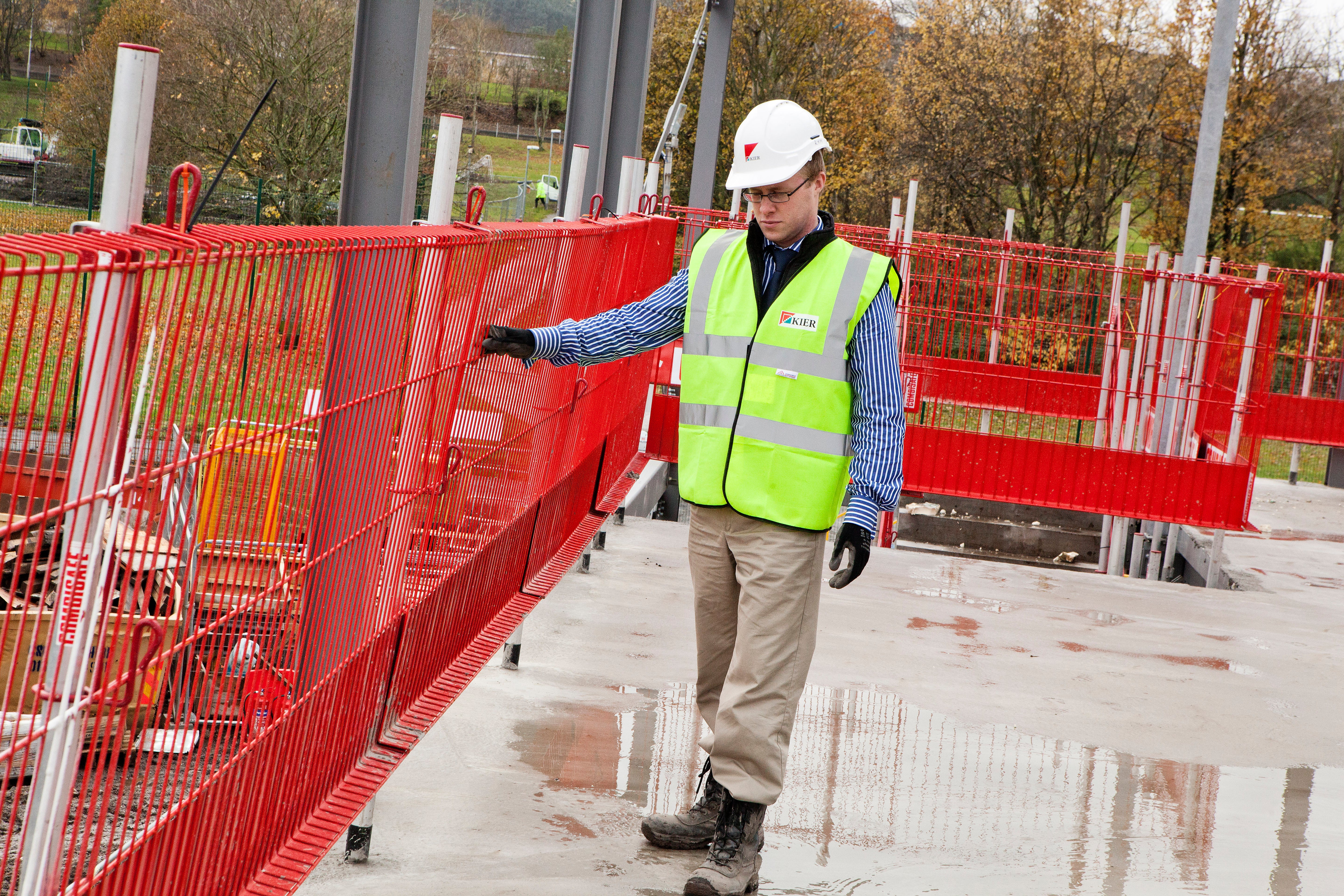 Person in safety gear standing on a construction site with red Combisafe barriers.